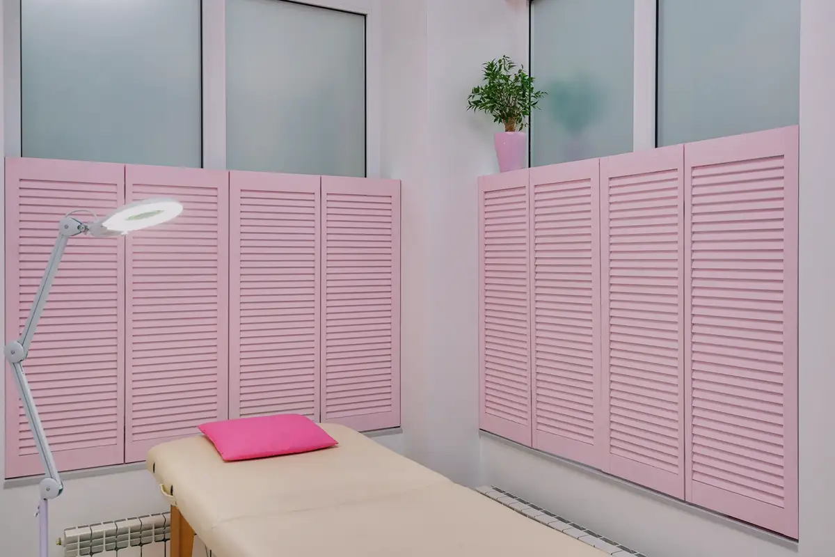 Treatment room with a padded bed, soft lamp and pink shutters