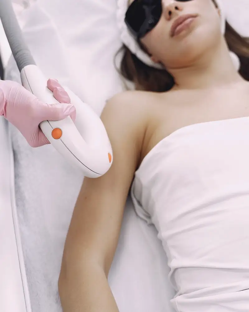 Gloved hands guiding a handheld laser device during a treatment in a bright clinic